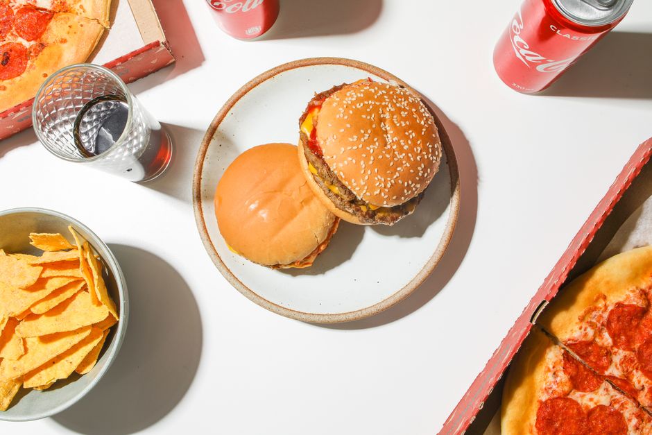 Top view of fast food spread with pizza, burgers, chips, and soda on a table.